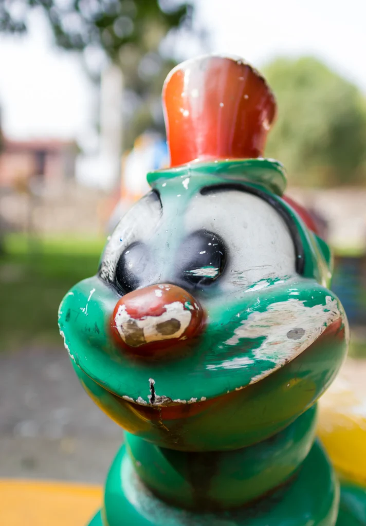 Worn clown figure on a playground ride with chipped green, red and white paint.